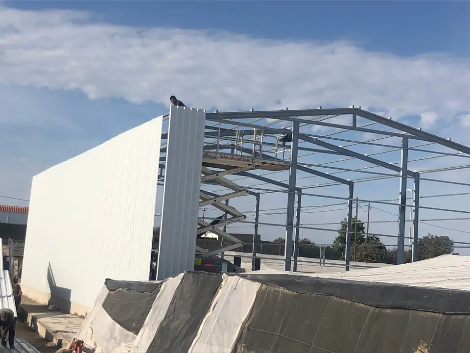 Operario colocando el cerramiento de chapa de una nave de estructura galvanizada junto a invernaderos