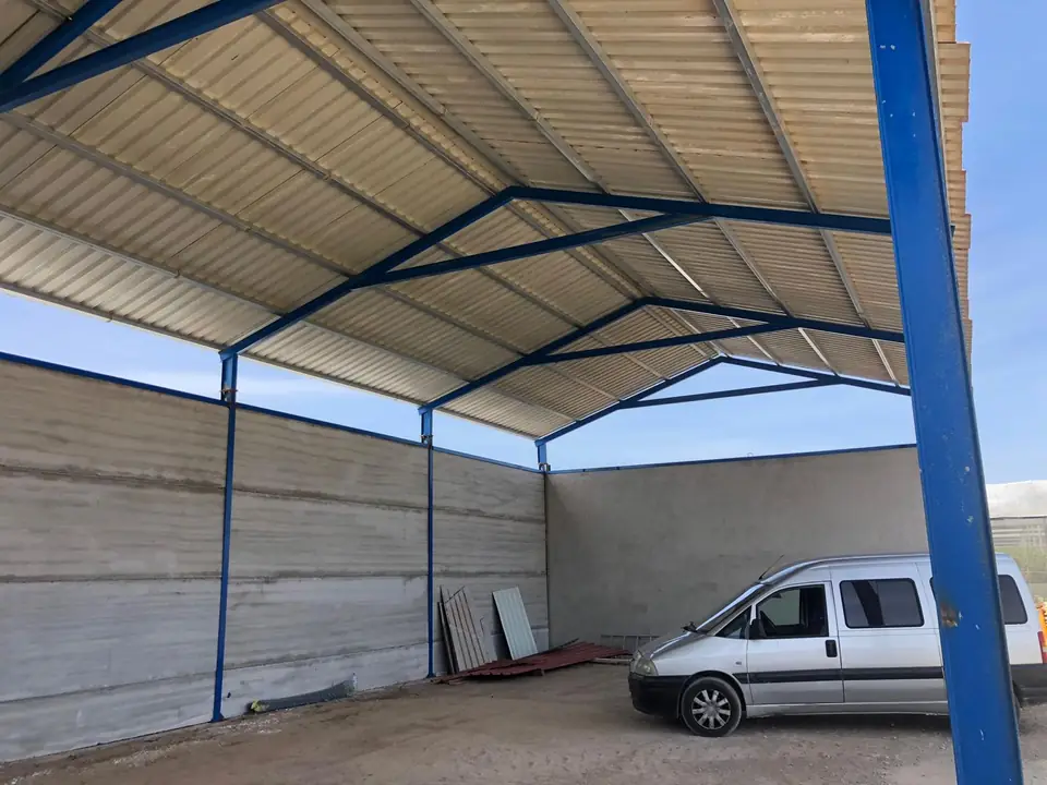Cobertizo agrícola con pórticos azules, cubierta de chapa y muros de hormigón