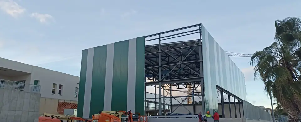 Edificio de estructura metálica con cerramiento de panel verde y blanco y plataformas elevadoras