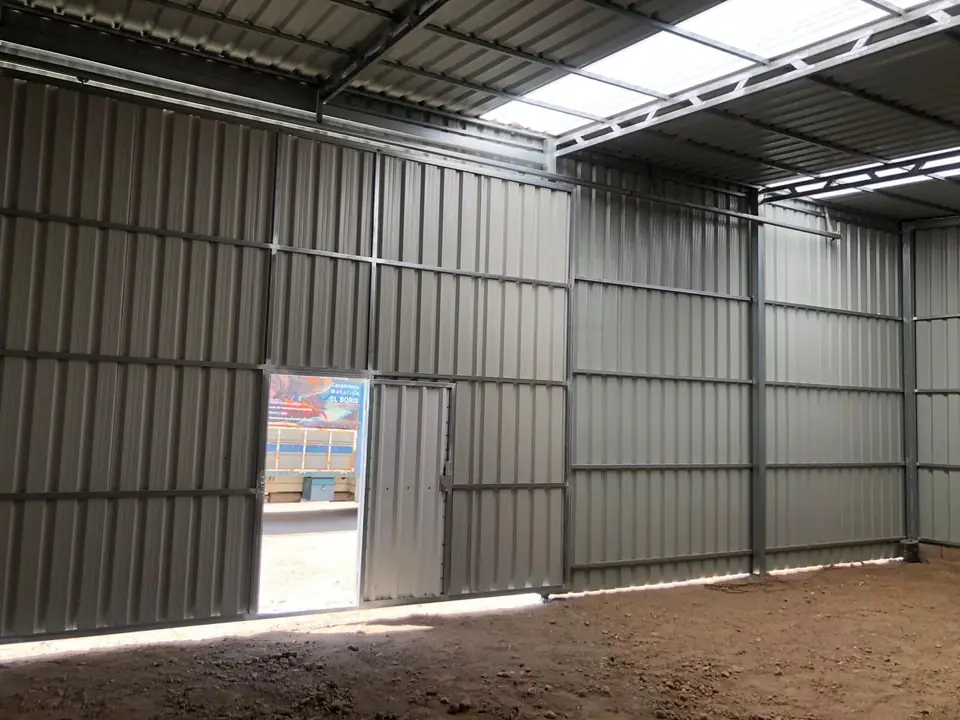 Interior de nave galvanizada con puerta peatonal abierta y el camión del taller fuera