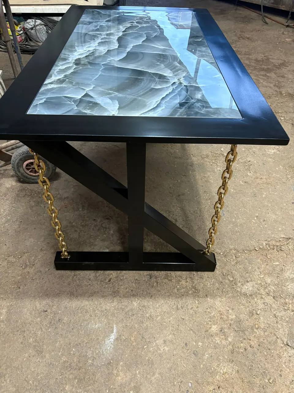 Mesa de acero lacado en negro con tablero de ónix y cadenas doradas, fabricada en el taller