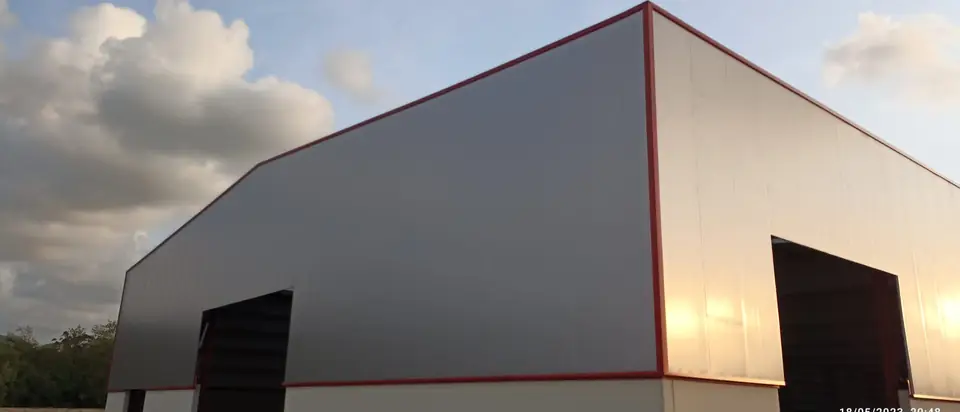 Nave de panel sándwich gris y blanco con remates rojos al atardecer