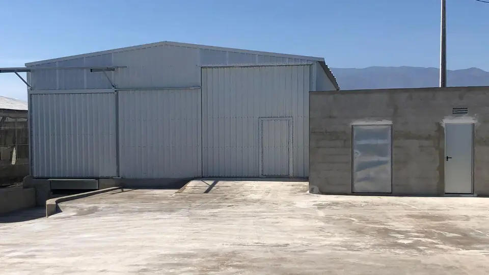 Nave metálica terminada con portón corredero y puerta peatonal, con la sierra al fondo